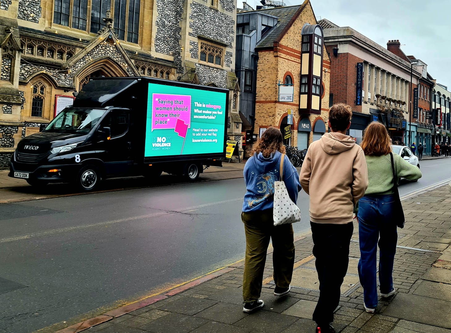 young people walking past and looking at ad van on side of road