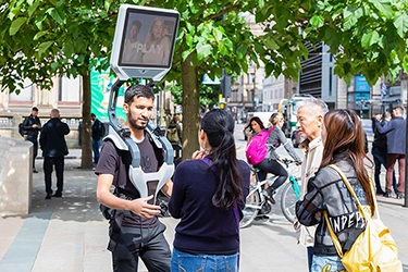 man wearing ad walker talking to member of the public